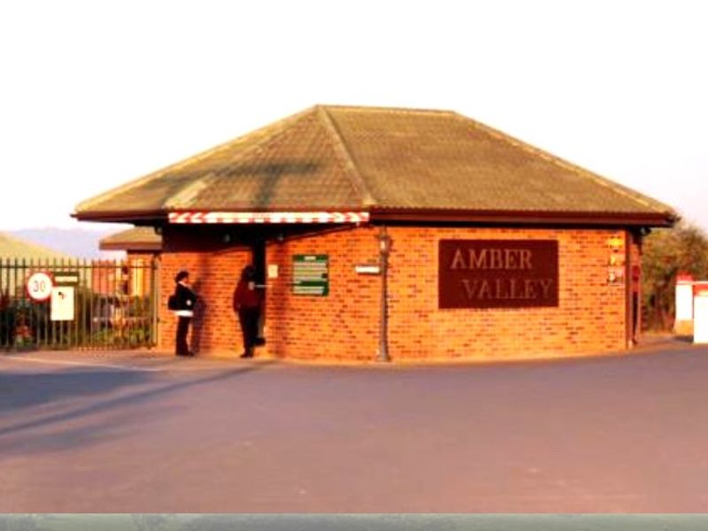 The entrance gate and security checkpoint for Amber Valley, featuring brick construction, tiled roofing, and controlled access boom gates.