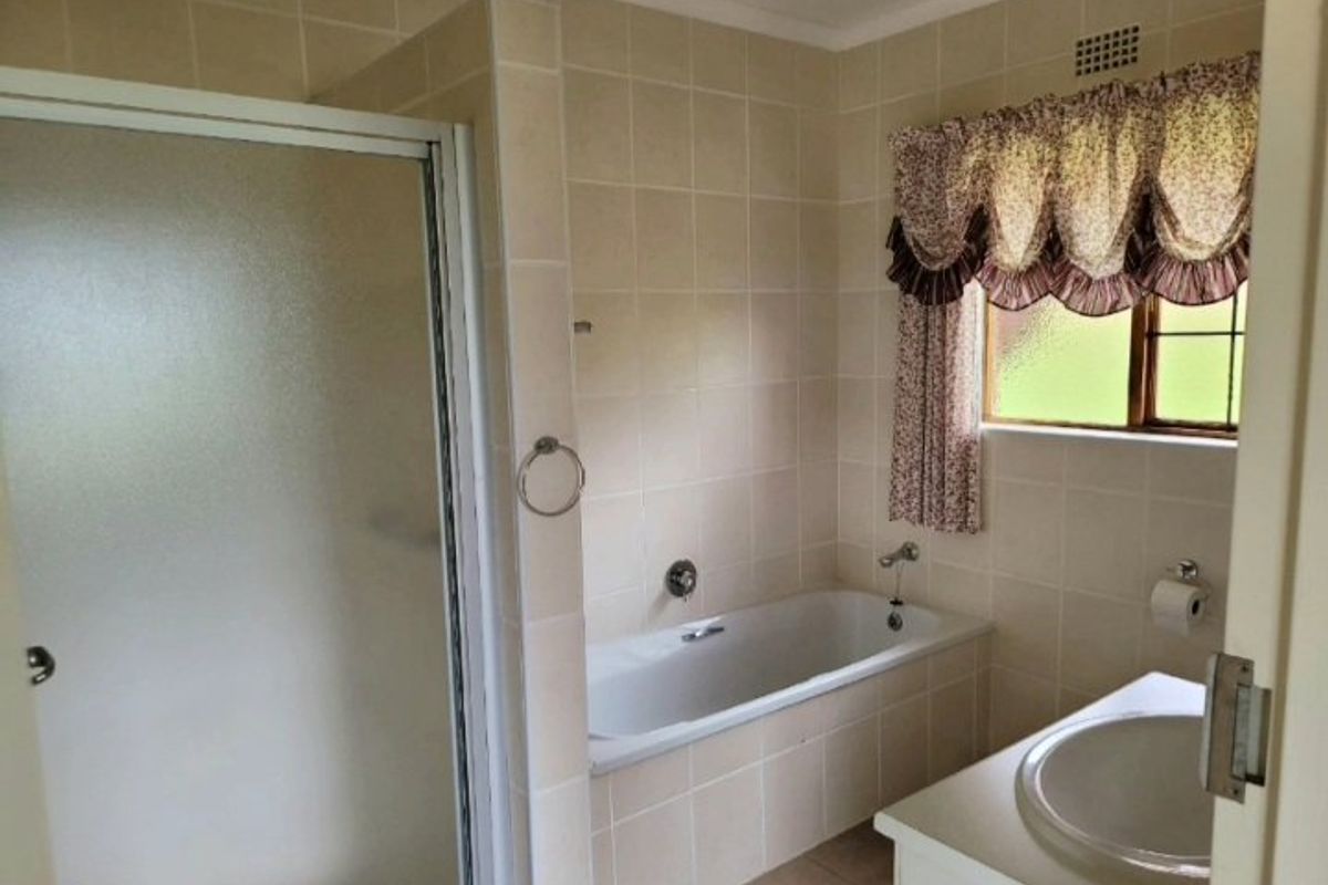 A functional bathroom featuring a built-in bathtub, separate shower enclosure, and a vanity basin with neutral wall tiling.