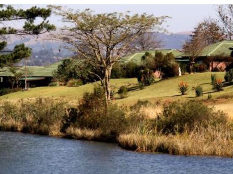 A scenic view of a tranquil lake with landscaped grounds and residential properties featuring pitched roofs in the background.