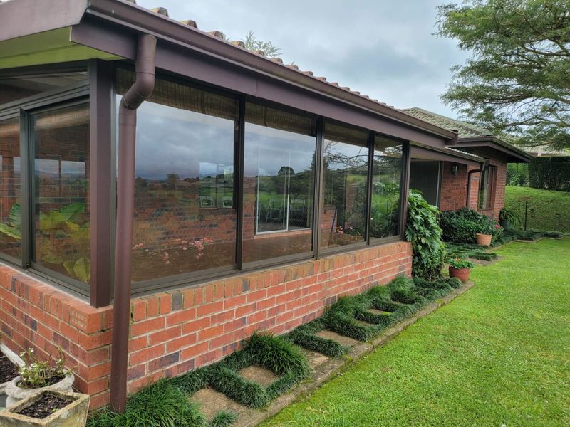 A covered patio area featuring brick construction, large sliding glass doors, and a tiled roof, overlooking a well-maintained garden.