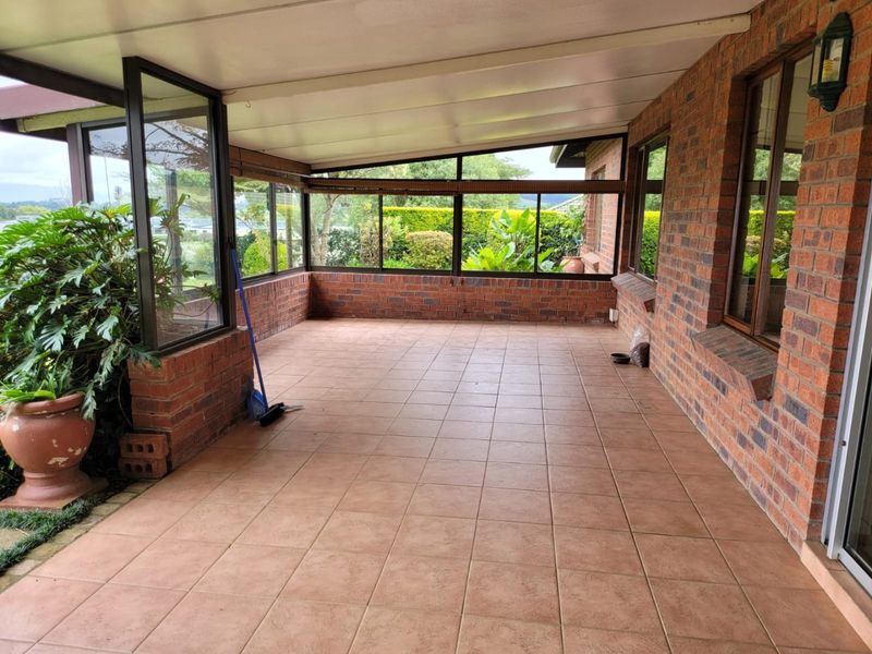 A spacious, covered patio area featuring brick walls, tiled flooring, and large windows overlooking the garden.