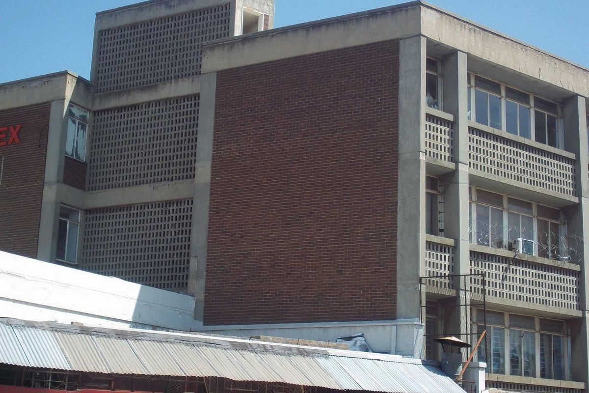 Exterior view of a multi-story commercial building featuring a brick and concrete facade with integrated breeze block ventilation screens and security fencing.