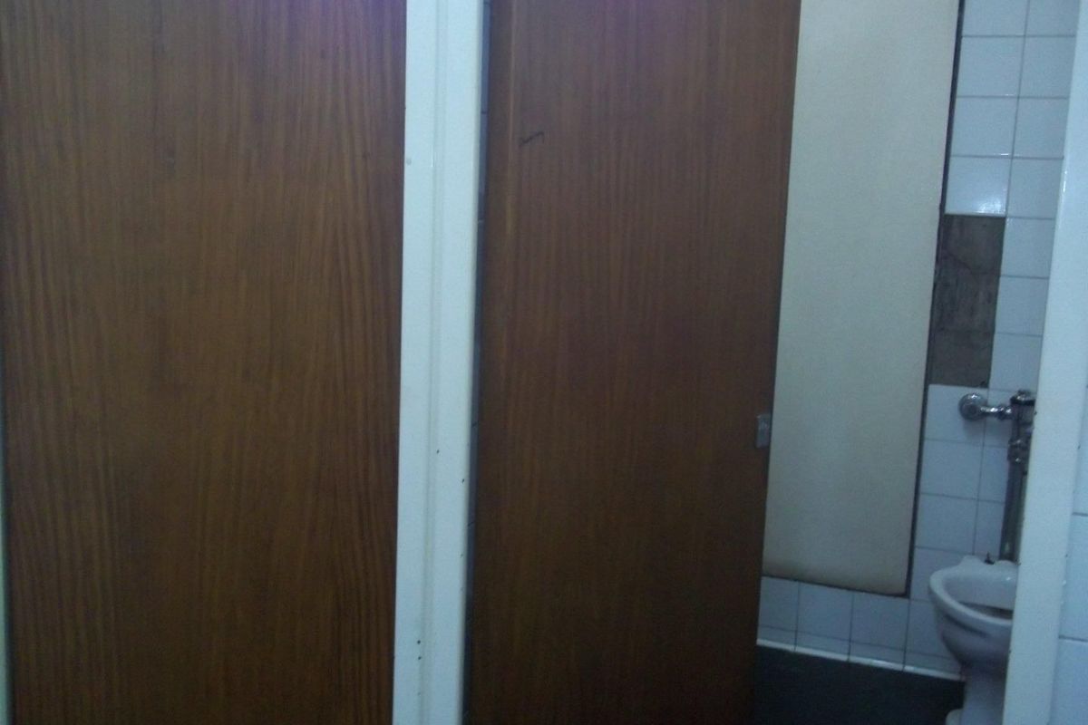 A commercial bathroom facility featuring wooden cubicle doors and tiled walls with visible maintenance requirements.