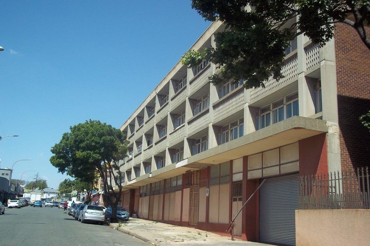 Street-level view of a multi-story commercial building featuring a concrete facade, brick accents, and a metal roller shutter entrance.