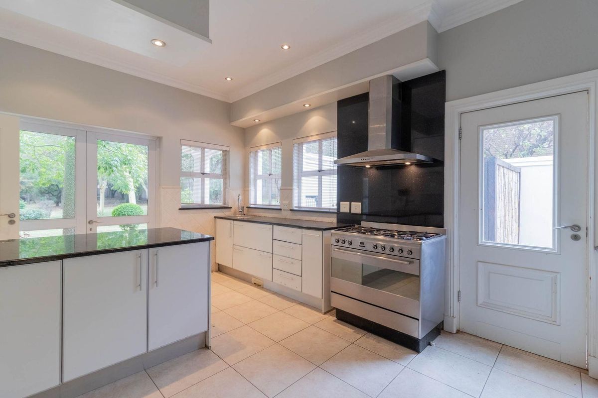 Modern kitchen featuring granite countertops, stainless steel gas stove, extractor fan, tiled flooring, and direct access to the garden through glass doors.