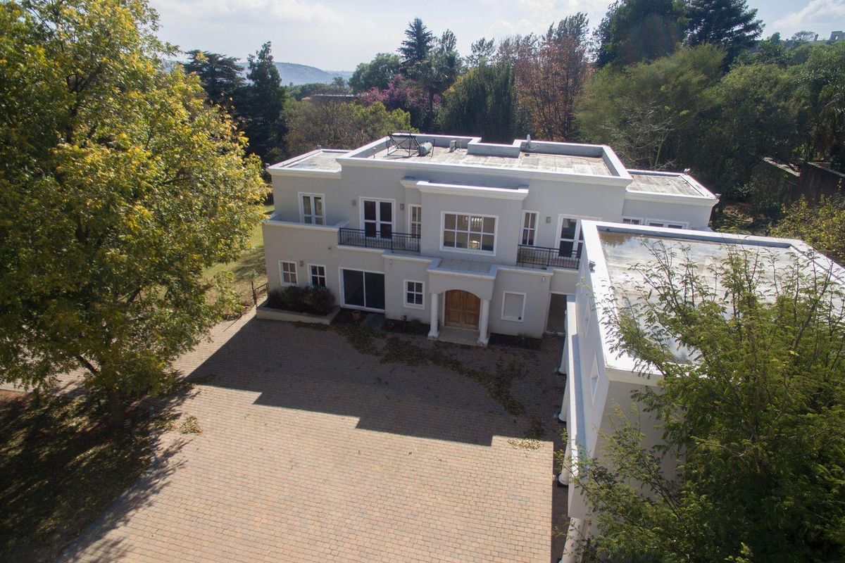 Aerial view of a double-storey residence featuring a paved driveway, multiple balconies, and a flat roof with solar geyser installation.