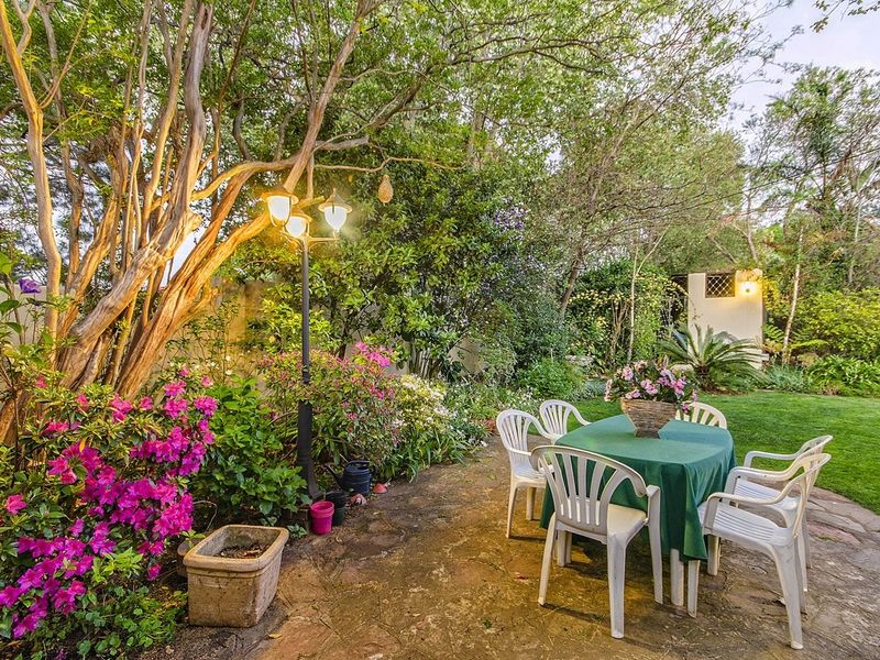 A lush, well-established garden featuring mature trees, vibrant flowering shrubs, stone paving, and integrated garden lighting, creating a serene outdoor setting.