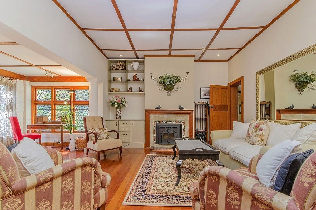 A cozy living room featuring a fireplace, built-in shelving, hardwood flooring, and distinctive timber ceiling beams with leaded glass windows.