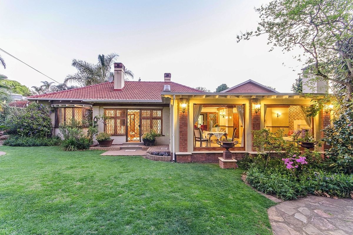 A charming rear elevation featuring a well-maintained garden, a covered patio area, and classic brick architecture with leaded glass windows.