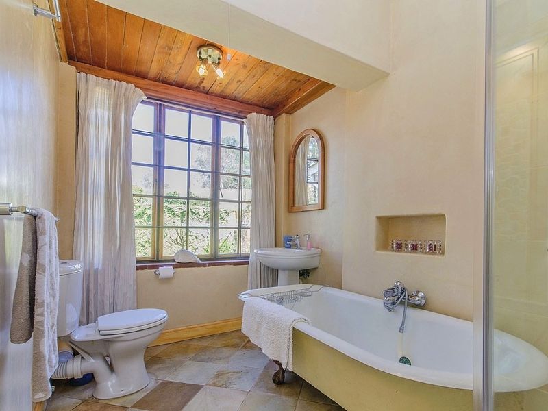 A characterful bathroom featuring a classic clawfoot bathtub, pedestal basin, separate shower enclosure, and warm timber ceiling with natural light.