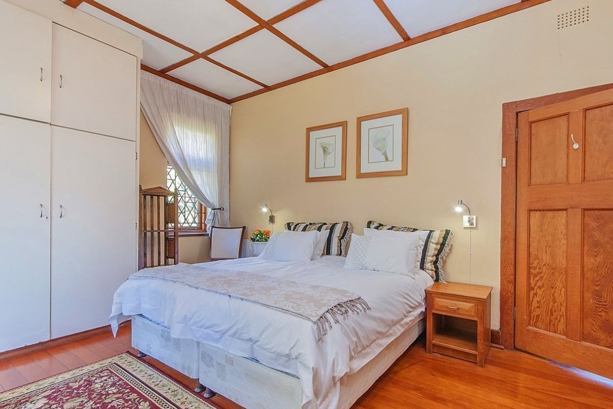 A cozy bedroom featuring warm timber flooring, a classic coffered ceiling, built-in storage cupboards, and a charming leaded glass window.