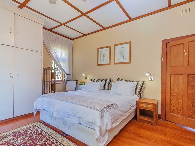 A cozy bedroom featuring warm timber flooring, a classic coffered ceiling, built-in storage cupboards, and a charming leaded glass window.