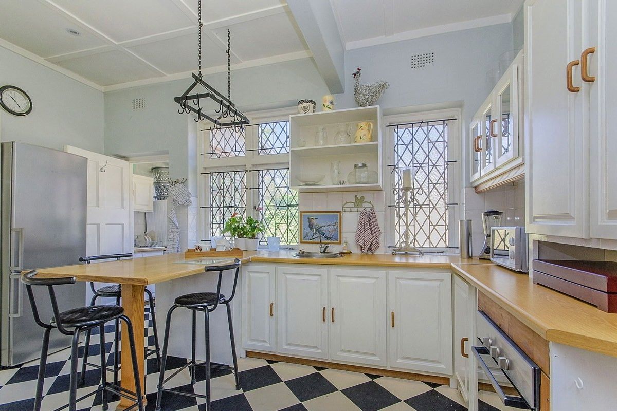 A charming kitchen featuring classic checkerboard flooring, wooden countertops, white cabinetry, and distinctive leaded glass windows with a built-in breakfast bar.
