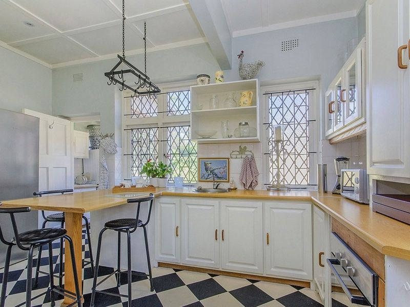 A charming kitchen featuring classic checkerboard flooring, wooden countertops, white cabinetry, and distinctive leaded glass windows with a built-in breakfast bar.