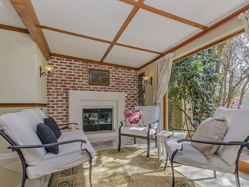Cozy living room featuring an exposed brick fireplace, timber ceiling beams, and large sliding glass doors providing natural light and garden views.