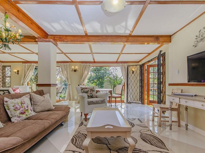 Spacious living room featuring exposed timber ceiling beams, polished tiled floors, and direct access to the garden through classic french doors.