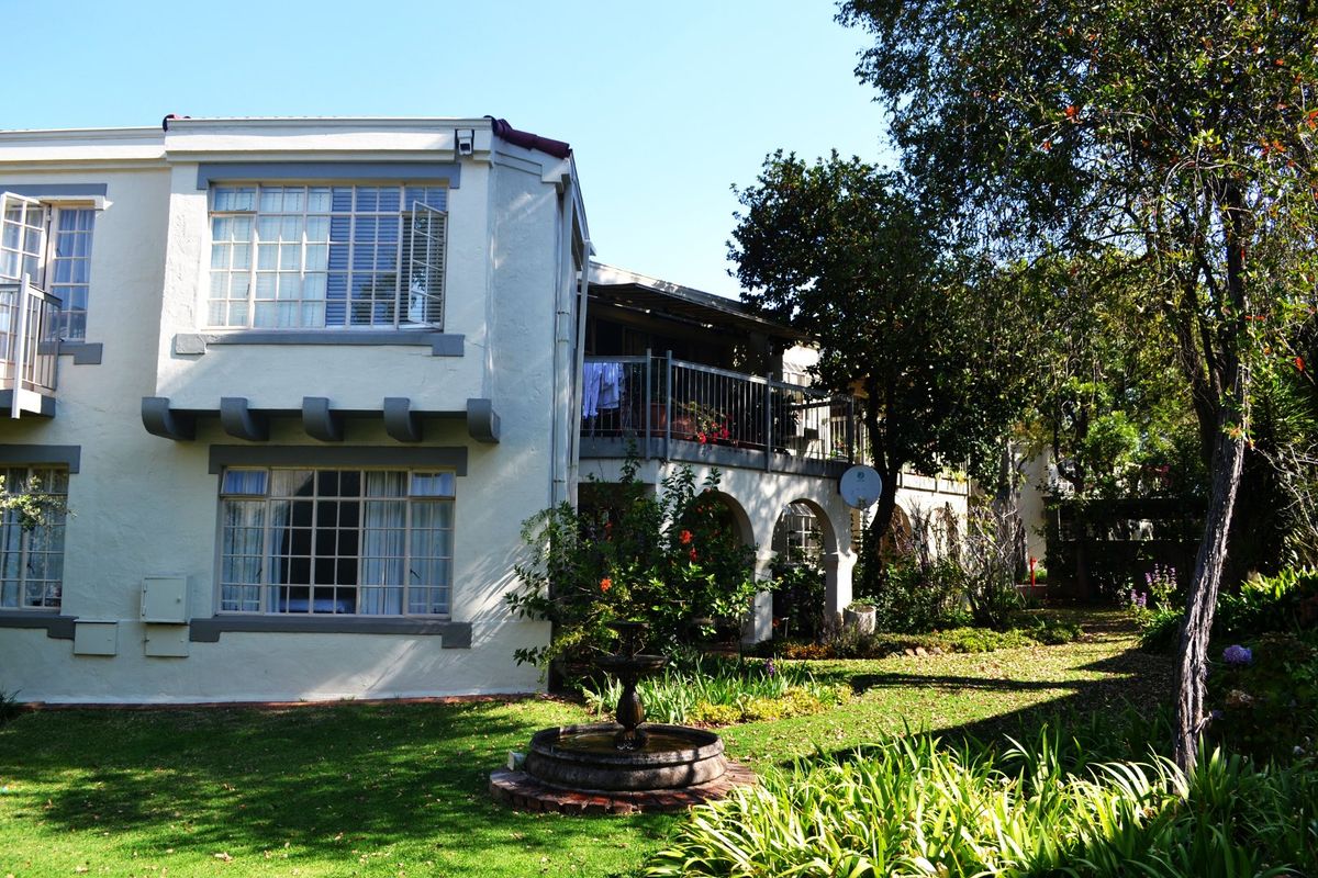 Rear view of the townhouse featuring a landscaped garden, stone fountain, and a balcony with metal railings overlooking the yard.