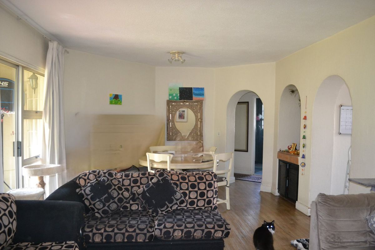 A living room featuring hardwood flooring, arched architectural doorways, and a sliding glass door providing access to the exterior.