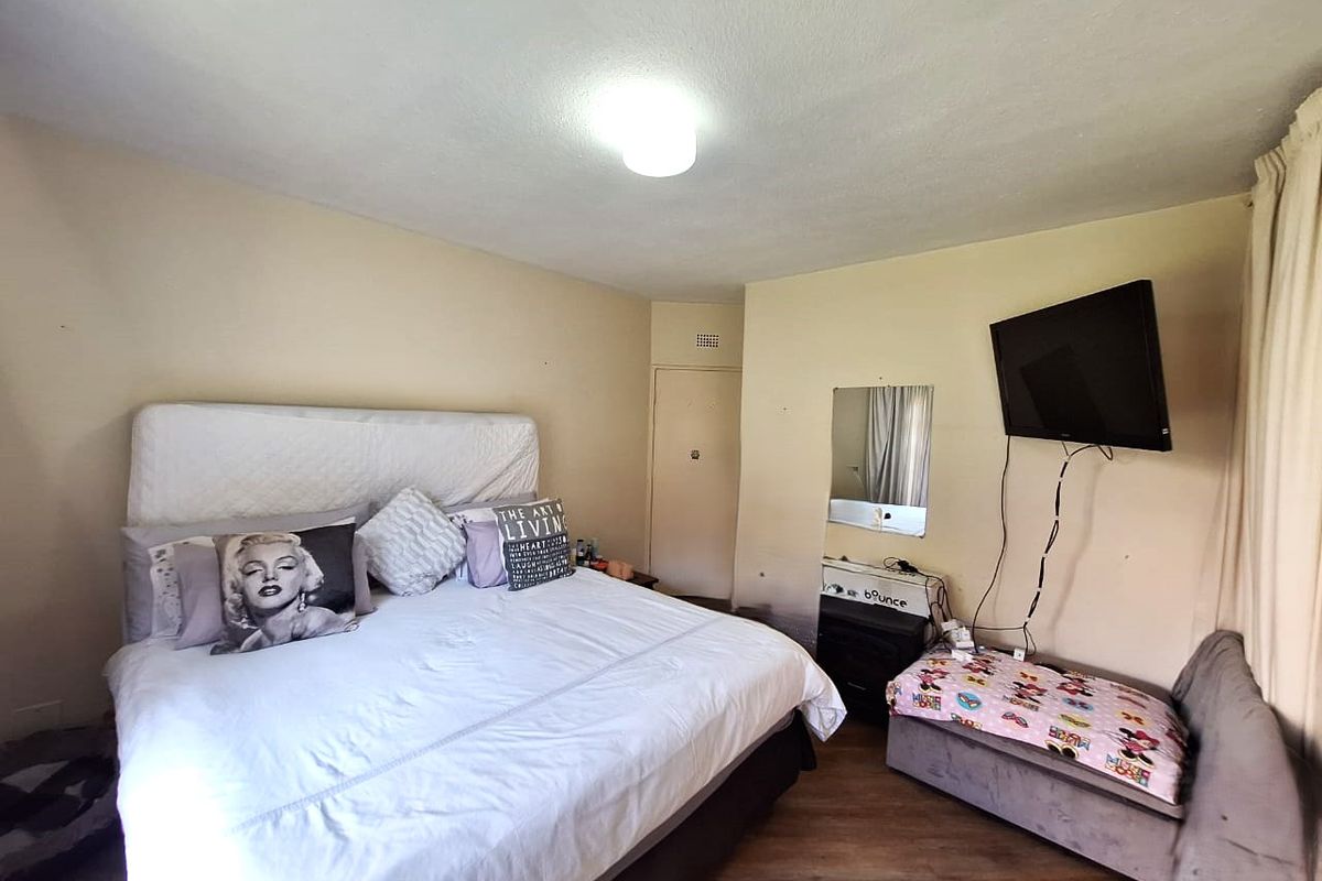 A bedroom featuring laminate flooring and neutral wall tones, equipped with a wall-mounted television bracket and a central ceiling light fixture.