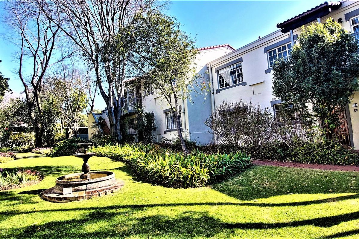 A well-maintained rear garden area featuring a stone fountain, lush lawn, and paved pathways leading to the townhouse facade.