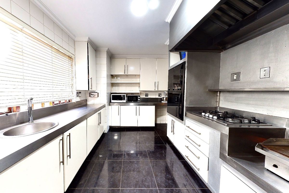 A functional galley-style kitchen featuring white cabinetry, stainless steel countertops, a gas hob, built-in oven, and dark tiled flooring.