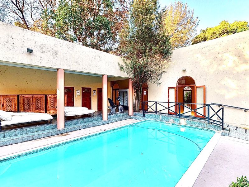 Outdoor pool area featuring a covered patio with concrete columns, tiled flooring, and direct access to the main building through arched doorways.