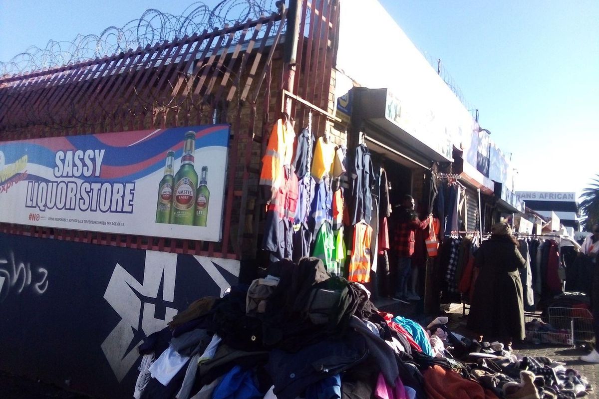 Street-level view of a commercial storefront featuring security fencing with razor wire, signage, and a roller shutter entrance.