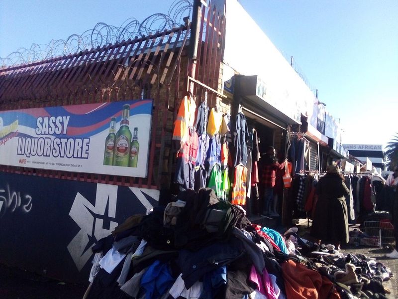Street-level view of a commercial storefront featuring security fencing with razor wire, signage, and a roller shutter entrance.