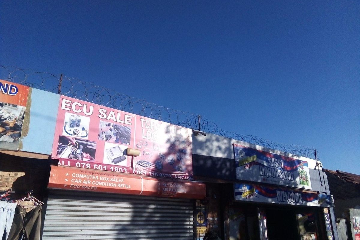 Front facade of a commercial property featuring roller shutter doors, prominent business signage, and perimeter security razor wire.