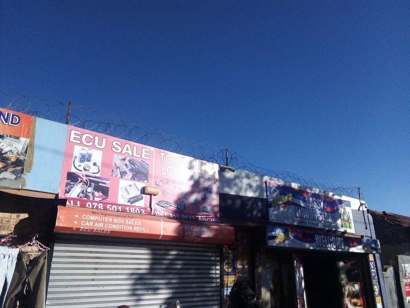 Front facade of a commercial property featuring roller shutter doors, prominent business signage, and perimeter security razor wire.