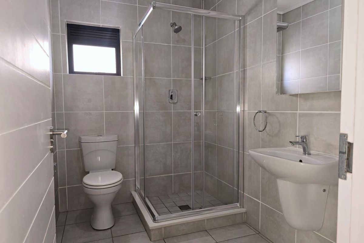 Modern bathroom featuring a glass-enclosed shower, pedestal basin, wall-mounted mirror, and neutral floor-to-ceiling tiling.