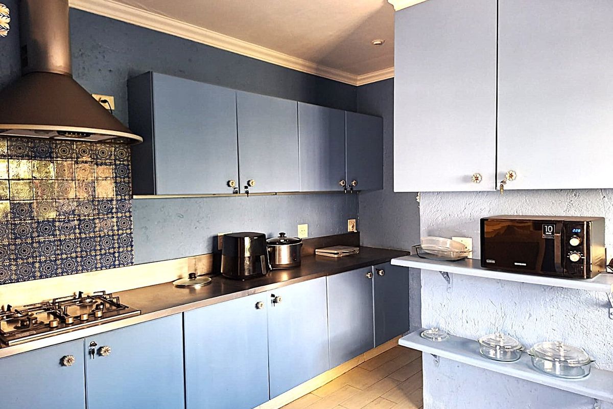 A functional kitchen featuring blue cabinetry, stainless steel countertops, a gas hob with extractor fan, and decorative tiled splashback.