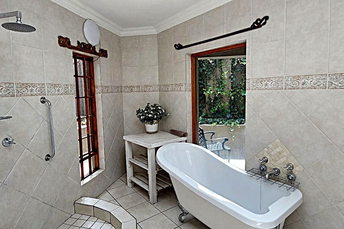 A bathroom featuring a freestanding bathtub, wall-mounted shower, and neutral wall tiling with decorative border accents, offering a functional and classic layout.