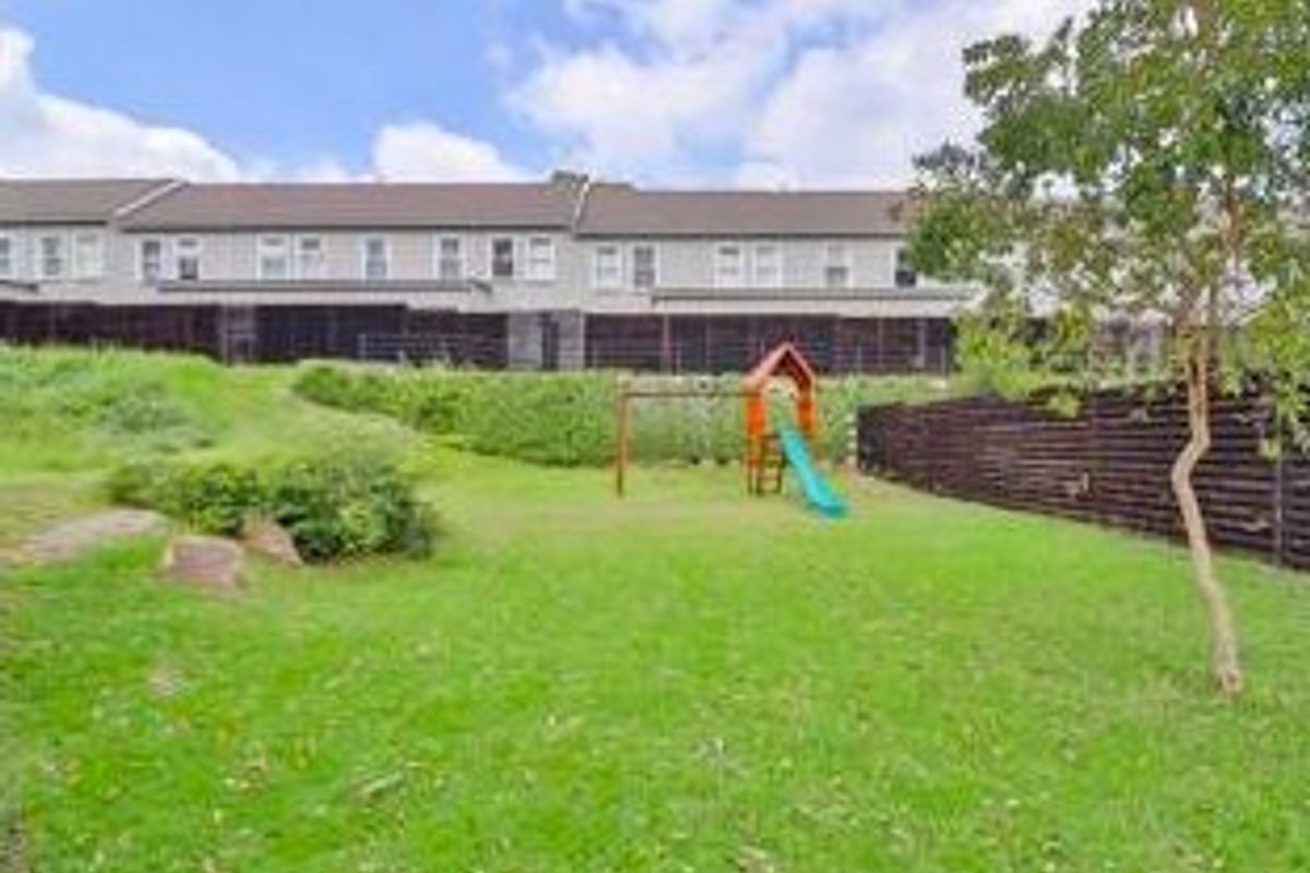 A rear view of the townhouse complex featuring a private grassed garden area with timber boundary fencing and a retaining wall.