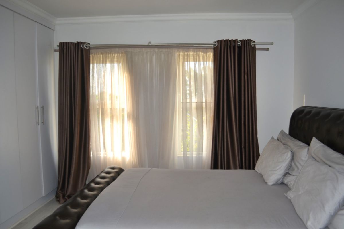 A well-maintained bedroom featuring a built-in wardrobe, neutral wall finishes, and window treatments.