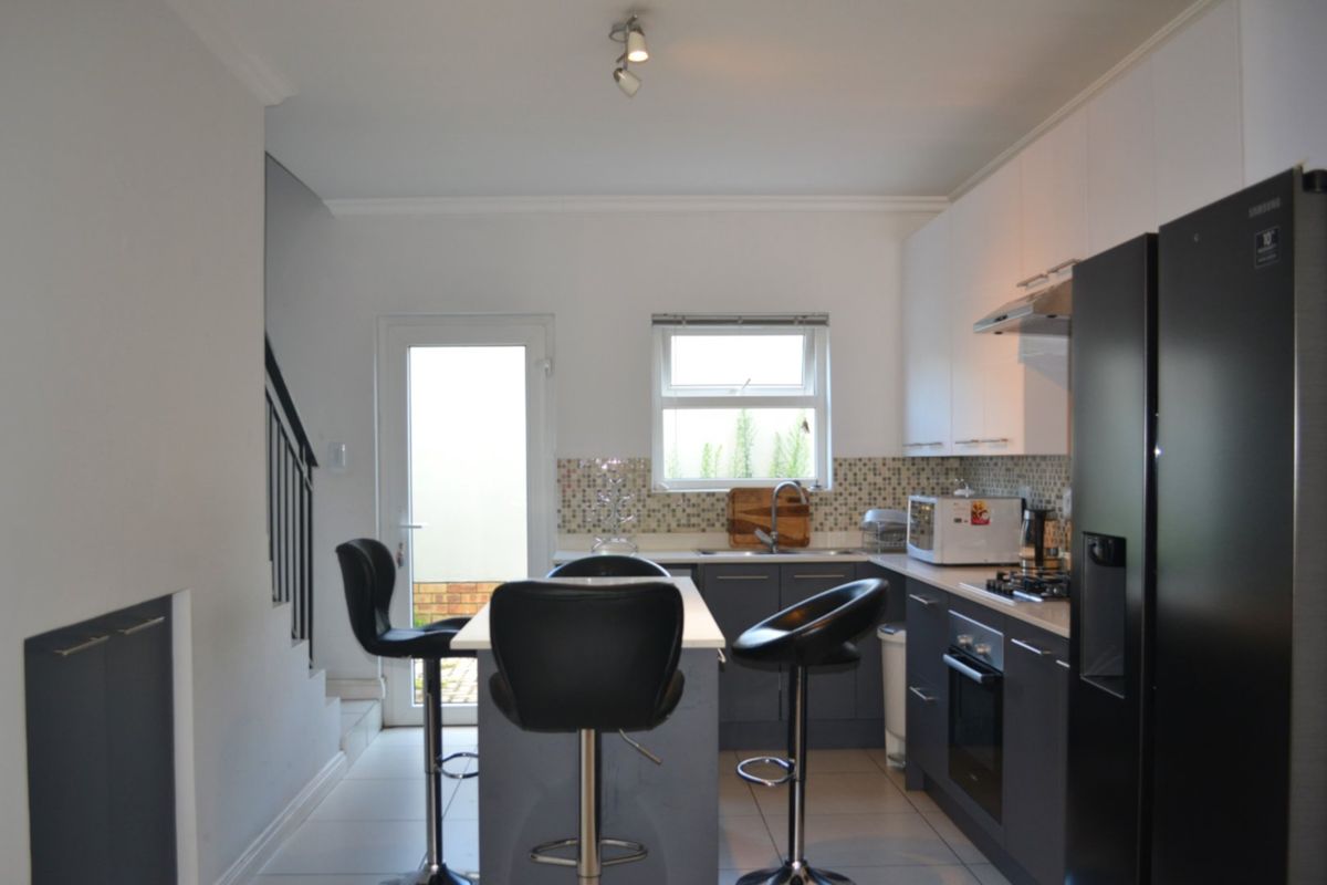 Modern kitchen featuring dark grey cabinetry, a central island, mosaic tile backsplash, and integrated appliances, with direct access to the rear exterior.