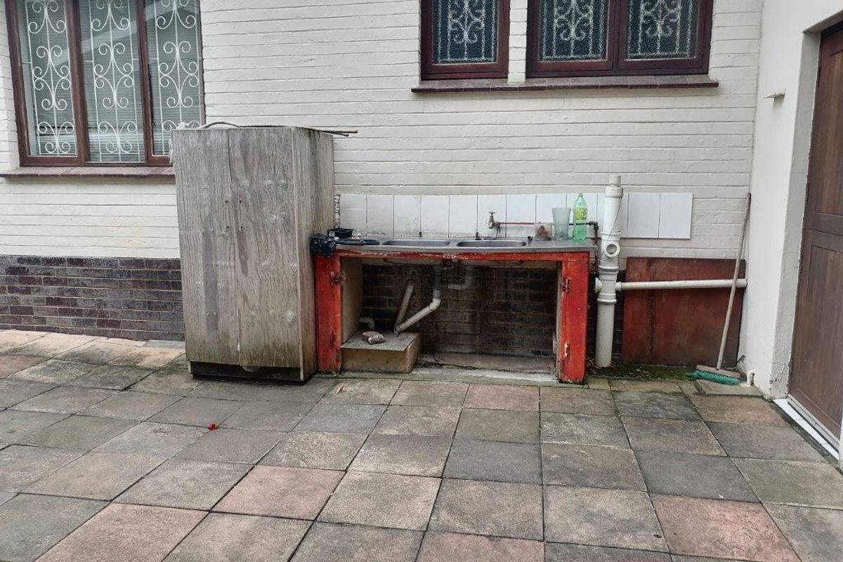 Rear exterior area featuring a paved patio and a basic outdoor sink station against a brick facade with security-barred windows.