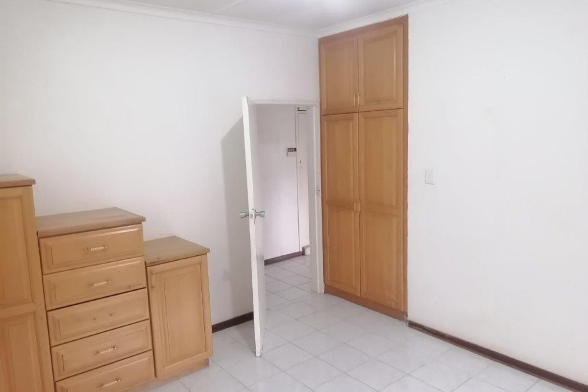 A bedroom featuring tiled flooring and built-in wooden cupboards, offering a functional and neutral space ready for personalization.