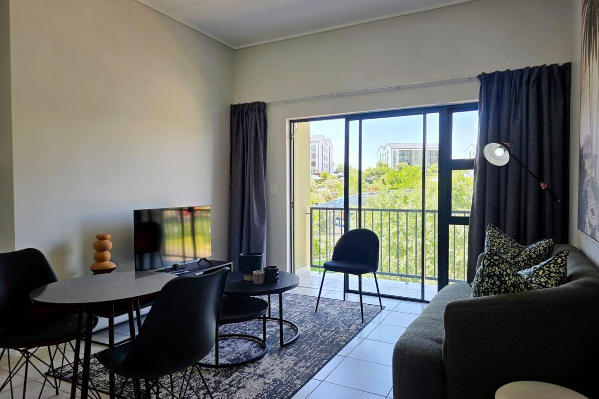A bright living room featuring tiled flooring and a large sliding glass door that opens onto a balcony with neighborhood views.