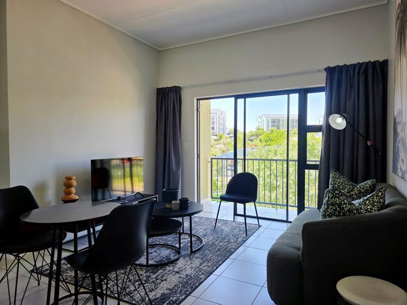 A bright living room featuring tiled flooring and a large sliding glass door that opens onto a balcony with neighborhood views.