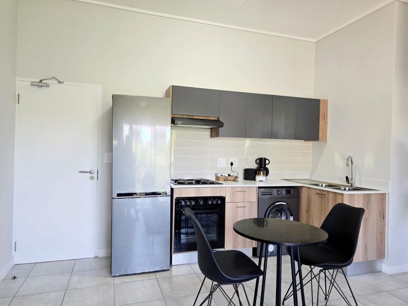 Modern open-plan kitchen featuring contemporary wood-grain and grey cabinetry, gas hob, built-in oven, and tiled flooring in a clean, well-maintained apartment setting.