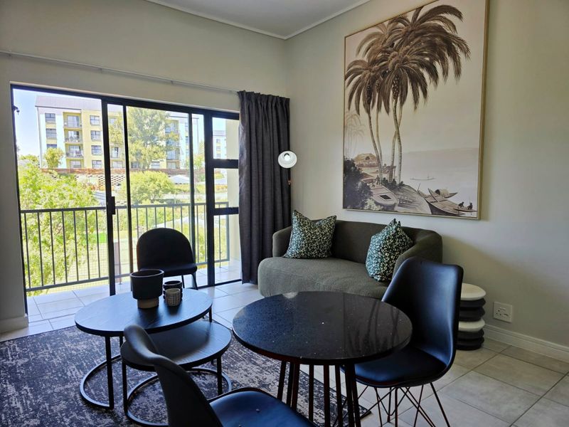 A bright living area featuring large sliding glass doors that open onto a balcony, providing natural light and views of the surrounding complex.