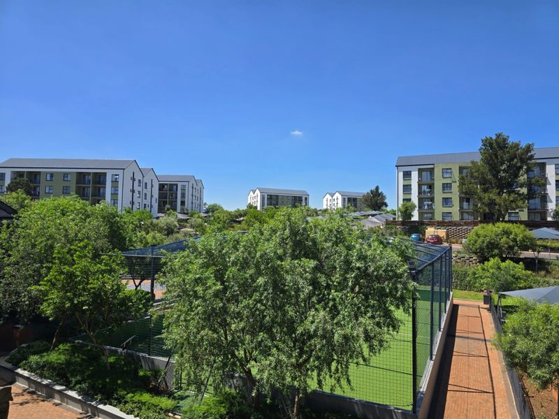 Elevated view overlooking a residential apartment complex featuring a fenced sports court, paved pathways, and established green landscaping.