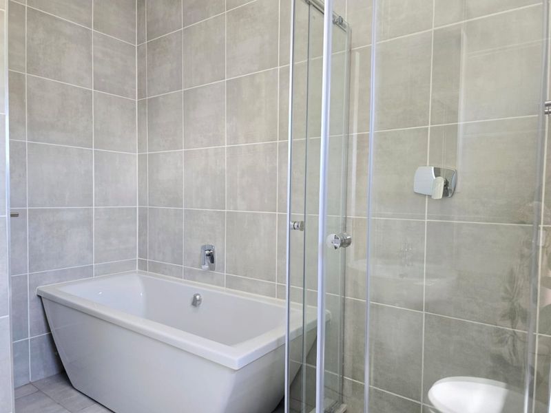 Modern bathroom featuring a sleek freestanding bathtub, a glass-enclosed shower, and contemporary grey ceramic wall tiling.