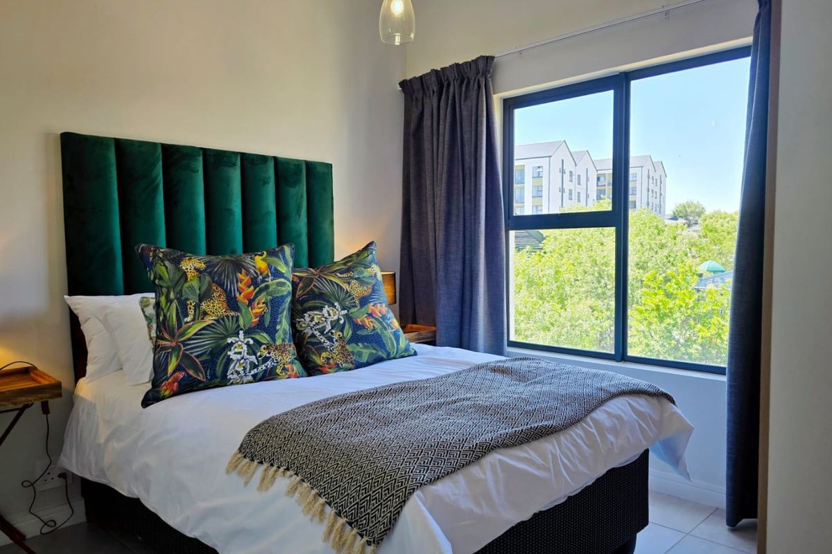 A well-lit bedroom featuring tiled flooring, a large aluminium-framed window, and a modern pendant light fixture.