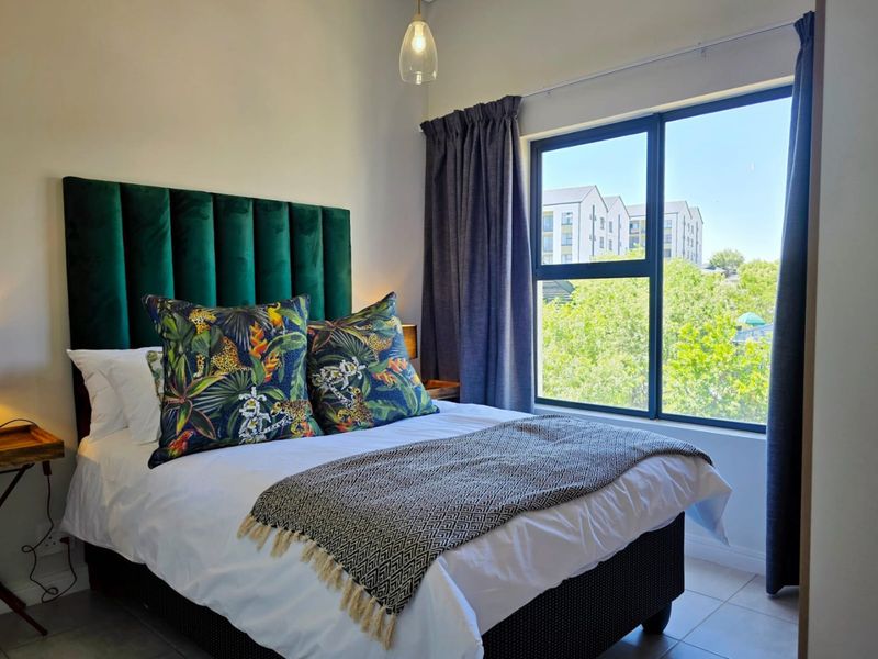 A well-lit bedroom featuring tiled flooring, a large aluminium-framed window, and a modern pendant light fixture.