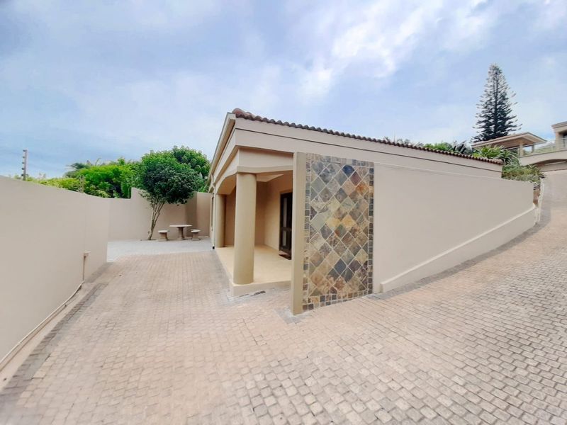 Front exterior view of the apartment featuring a paved driveway, stone-clad accent wall, and covered entrance area with structural columns.