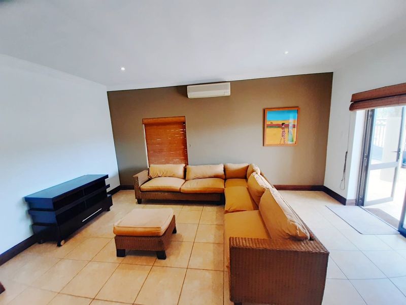 A spacious living room featuring tiled flooring, recessed lighting, an integrated air conditioning unit, and direct access to an outdoor area via a sliding door.
