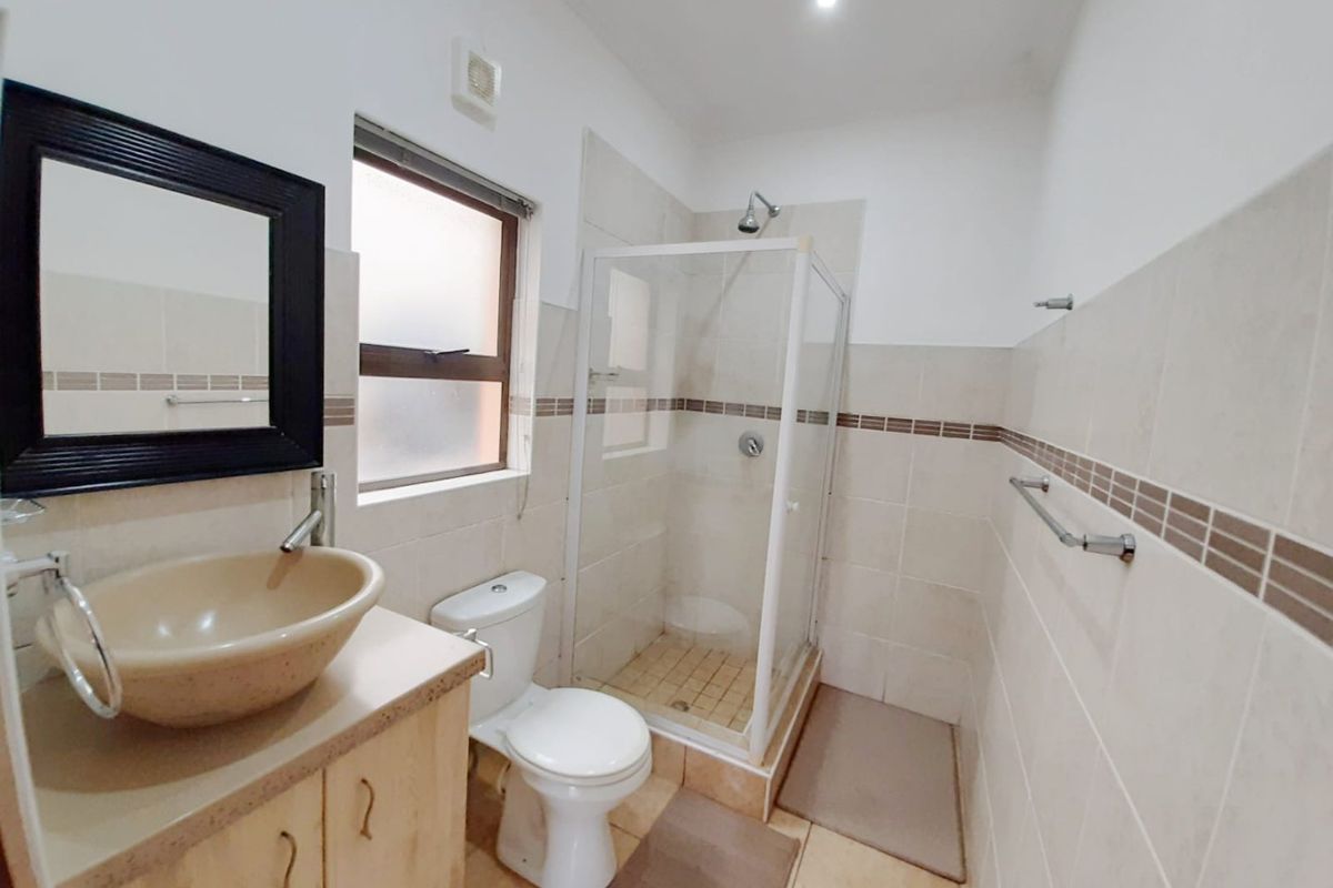 A functional bathroom featuring a shower enclosure, toilet, and a vanity with a vessel sink, finished with neutral wall and floor tiling.