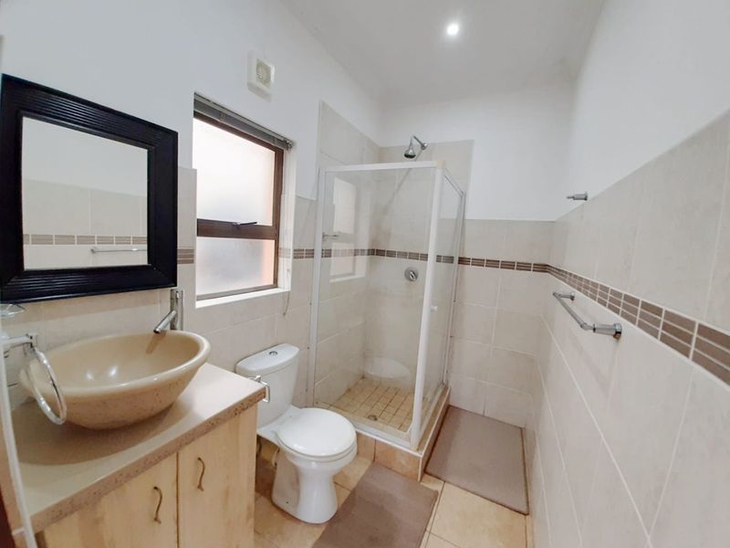 A functional bathroom featuring a shower enclosure, toilet, and a vanity with a vessel sink, finished with neutral wall and floor tiling.